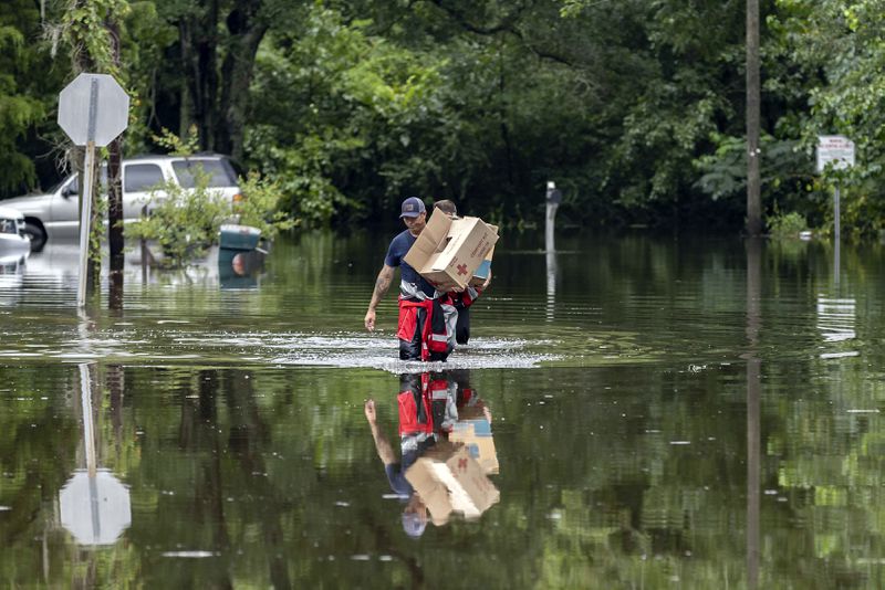 Savannah Firefighters Andrew Stevenson (front) and Ron Strauss carry food to residents in the Tremont Park neighborhood that was hit by flooding from Hurricane Debby on Tuesday, Aug. 6, 2024, in Savannah, Ga. (Stephen B. Morton/AP)